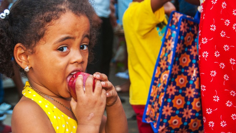 Niña disfruta de comer una manzana en puesto de frutas avenida Mella casi esquina Duarte